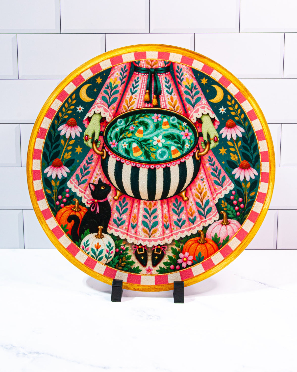 Brewed for You round Halloween glass cutting board with a pink-dressed witch, striped bubbling cauldron, black cat, pumpkins, flowers, candy corn, moons and stars.